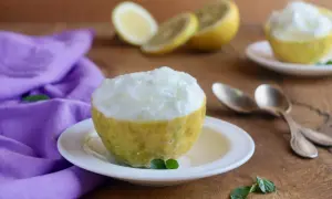 Sorbetto al limone senza albume servito in un limone scavato, con limoni affettati e un tovagliolo viola sullo sfondo.