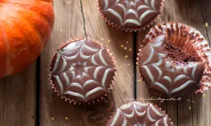 Muffin Halloween facili con decorazione a ragnatela. Una zucca arancione e stelline dorate completano la scena.