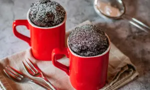 Due tortine al cioccolato in tazza, spolverate di zucchero a velo, pronte per essere gustate. Una delizia veloce da preparare al microonde.