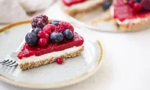 Una fetta di cheesecake ai frutti di bosco, con una glassa rossa brillante e bacche fresche, su un piatto con una forchetta.