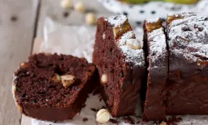 Fetta di banana bread cacao con nocciole e zucchero a velo, su tagliere di legno.