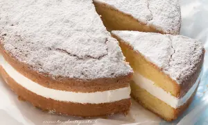 Una soffice torta kinder paradiso, spolverata di zucchero a velo, con una golosa crema bianca tra due strati di pan di Spagna.