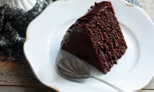 Una fetta di torta al cioccolato, ricca e umida, su un piatto bianco con un cucchiaino d'argento.