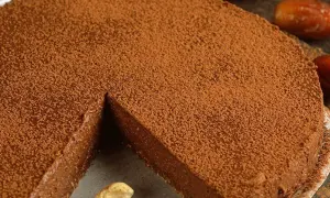Torta al cioccolato spolverata di cacao, con una fetta mancante e anacardi a guarnire.