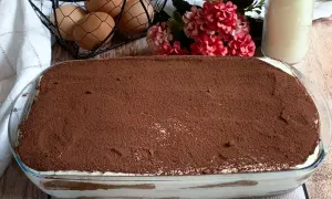 Tiramisù pronto, con 500 g di mascarpone, pronto per essere gustato. Ingredienti freschi come uova e fiori decorano la tavola.