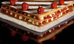 Una magnifica torta millefoglie con strati di pasta sfoglia, crema pasticcera e fragole fresche, decorata con fragole intere e zucchero a velo.