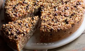 Una deliziosa torta di nocciole, ricoperta di granella croccante e gocce di cioccolato, con una fetta tagliata.