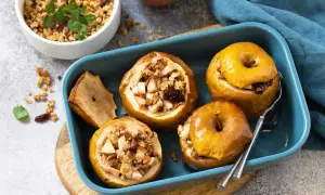 Mele cotte ripiene di frutta secca e granola, servite in una teglia blu.