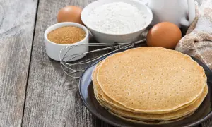 Ingredienti per la ricetta crepes: farina, uova, zucchero, latte e frusta su un tavolo di legno.