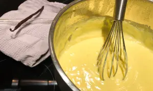 Crema pasticcera senza latte in preparazione, con bacca di vaniglia e frusta.