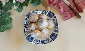 Piatto di ravioli al cioccolato spolverati di zucchero a velo, decorato con fiori e foglie verdi.