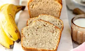 Fetta di banana bread senza uova, soffice e dorata, accanto a banane mature e un bicchiere di latte.