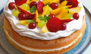 Torta con pan di spagna, panna montata e frutta fresca: uva, pesche e prugne. Un dolce estivo colorato e invitante.