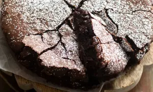 Torta con 2 uova e cioccolato fondente, spolverata di zucchero a velo, con una fetta sollevata che rivela la sua morbidezza.