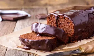 Plumcake al cioccolato con glassa lucida e due fette tagliate, su carta da forno e legno.