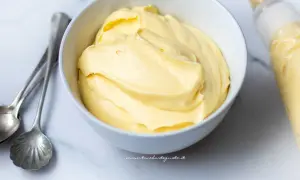Crema chantilly soffice in una ciotola, pronta per decorare una torta. Accanto, cucchiaini d'argento e una sac à poche.