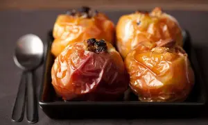 Mele cotte in friggitrice ad aria, caramellate e ripiene di uvetta e mandorle, pronte per essere gustate con un cucchiaio.