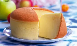 Una soffice torta di cotone, dorata e leggera, servita su un piatto con mele verdi e rosse sullo sfondo.