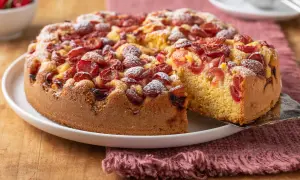Torta con ciliegie, soffice e profumata, cosparsa di zucchero a velo. Una fetta viene sollevata, mostrando la morbidezza dell'impasto.