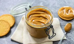 Vaso di vetro pieno di cremoso dulce de leche, con biscotti e un cucchiaino pronto per assaporare questa delizia.