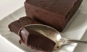 Una mattonella di cioccolato fondente, densa e lucida, su un piatto bianco. Un cucchiaino ne ha prelevato un pezzo.
