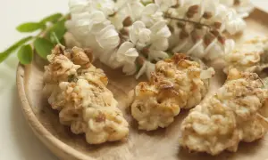 Fiori di acacia fritti dorati su un piatto di legno, con grappoli di fiori freschi sullo sfondo.