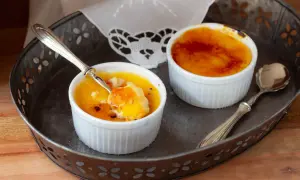 Due deliziosi creme brulee in cocotte, uno con un cucchiaino che ne assaggia la crosticina caramellata.