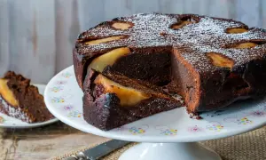 Deliziosa torta pere e cioccolato, con una fetta tagliata e cosparsa di zucchero a velo.