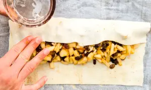 Mani che chiudono uno strudel di mele con pasta sfoglia, ripieno di mele a cubetti, uvetta e pinoli.