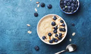 Porridge ricetta: una ciotola di avena con mirtilli, banane e mandorle a lamelle su sfondo blu.
