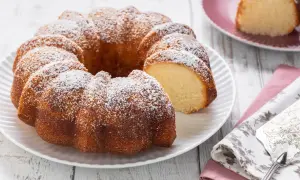 Ciambellone senza uova, soffice e dorato, spolverato di zucchero a velo. Una fetta è già stata tagliata, invitando ad assaggiarlo.