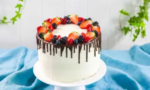Torta bianca con glassa al cioccolato che cola, decorata con fragole, mirtilli e lamponi freschi. Un drip cake perfetto per ogni occasione.