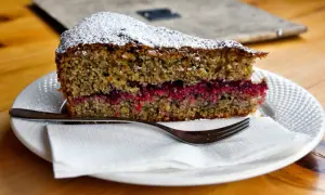Una fetta di torta con farina di grano saraceno e cioccolato, farcita con marmellata di frutti rossi, spolverata di zucchero a velo.
