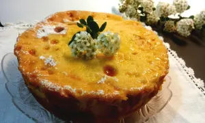 Deliziosa torta di riso massese, dorata e lucida, decorata con fiori bianchi e spolverata di zucchero a velo.