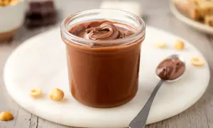 Un vasetto pieno di deliziosa nutella fatta in casa, con nocciole e cioccolato a vista.