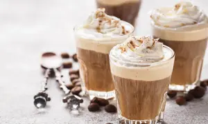 Tre bicchieri di deliziosa crema al caffè, guarniti con panna montata e cacao, circondati da chicchi di caffè.