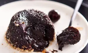Tortino cuore caldo con cioccolato fuso che cola, perfetto per una ricetta infallibile. Un ciliegino completa il piatto.