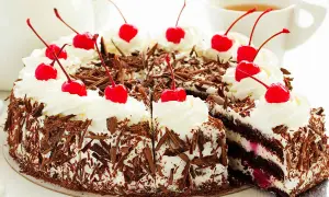Una deliziosa foresta nera torta, ricoperta di panna montata e ciliegie rosse, con scaglie di cioccolato che la rendono irresistibile.