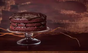 Torta a tre strati di torte al cioccolato, ricoperta da glassa lucida al cioccolato, su un'alzata di vetro.
