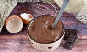Crema pasticcera al cioccolato, liscia e invitante, pronta per essere gustata. Uova, frusta e cioccolato, ingredienti per un dolce momento.