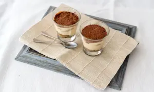 Due bicchierini di tiramisù con colomba, cosparsi di cacao, su un runner di iuta.