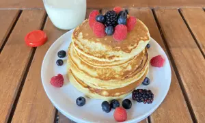 Pancake light con frutti di bosco e un bicchiere di latte su un tavolo di legno.