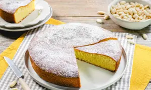 Deliziosa torta con farina di mandorle, spolverata di zucchero a velo, con una fetta tagliata. Accanto, una ciotola di mandorle.
