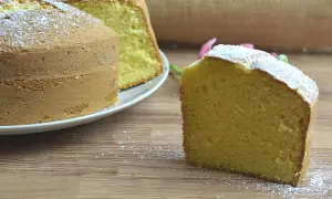 Un ciambellone soffice, spolverato di zucchero a velo, attende di essere gustato. Una fetta è già pronta sul tavolo di legno.