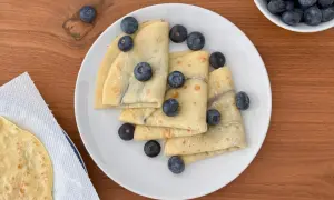 Deliziose crepes all'acqua, piegate e guarnite con mirtilli freschi, su un piatto bianco.