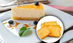 Una fetta di cheesecake con topping giallo, mirtilli e salsa caramello, accompagnata da biscotti secchi. Diversi tipi di cheesecake per ogni gusto.