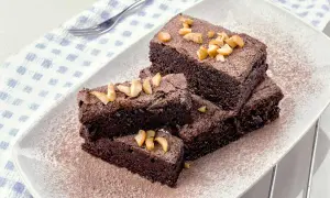 Fette di torta al cioccolato e nocciole, spolverate di cacao e guarnite con nocciole tritate, su un piatto bianco.