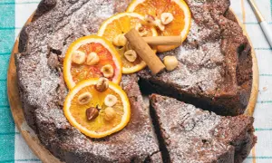 Torta di pane ricetta della nonna, cosparsa di zucchero a velo, decorata con fette d'arancia, nocciole e cannella.