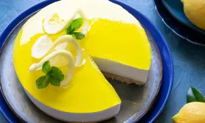 Cheesecake lime lucido con decorazioni di limone e menta, una fetta è stata tolta.