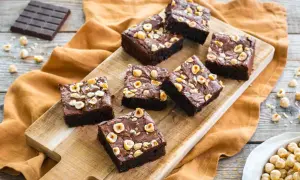 Deliziosi brownies senza glutine con nocciole tostate, disposti su un tagliere di legno.